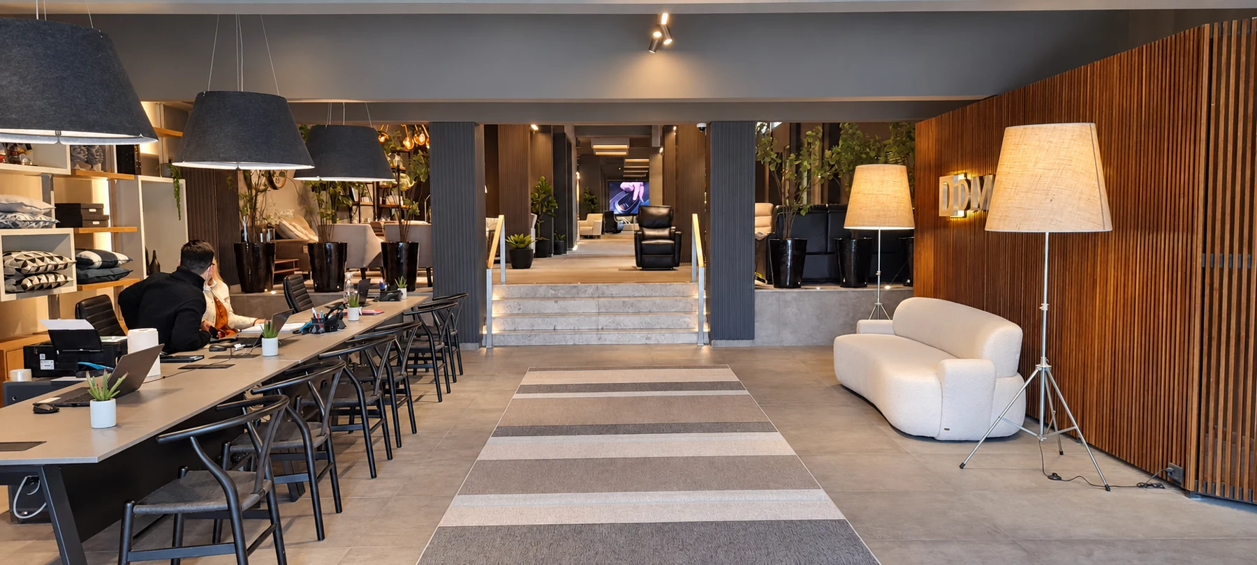 Entrada renovada del showroom con escritorios de atención a la izquierda, escalones centrales y pared de madera a la derecha
