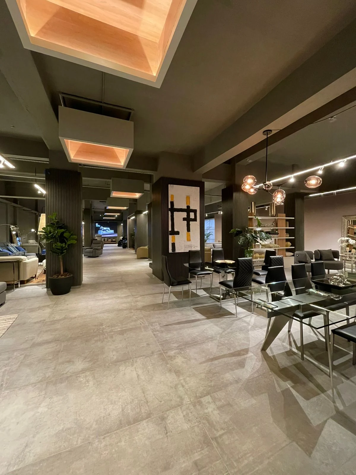 Recorrido longitudinal del showroom con columnas oscuras revestidas, mesas y luminarias suspendidas