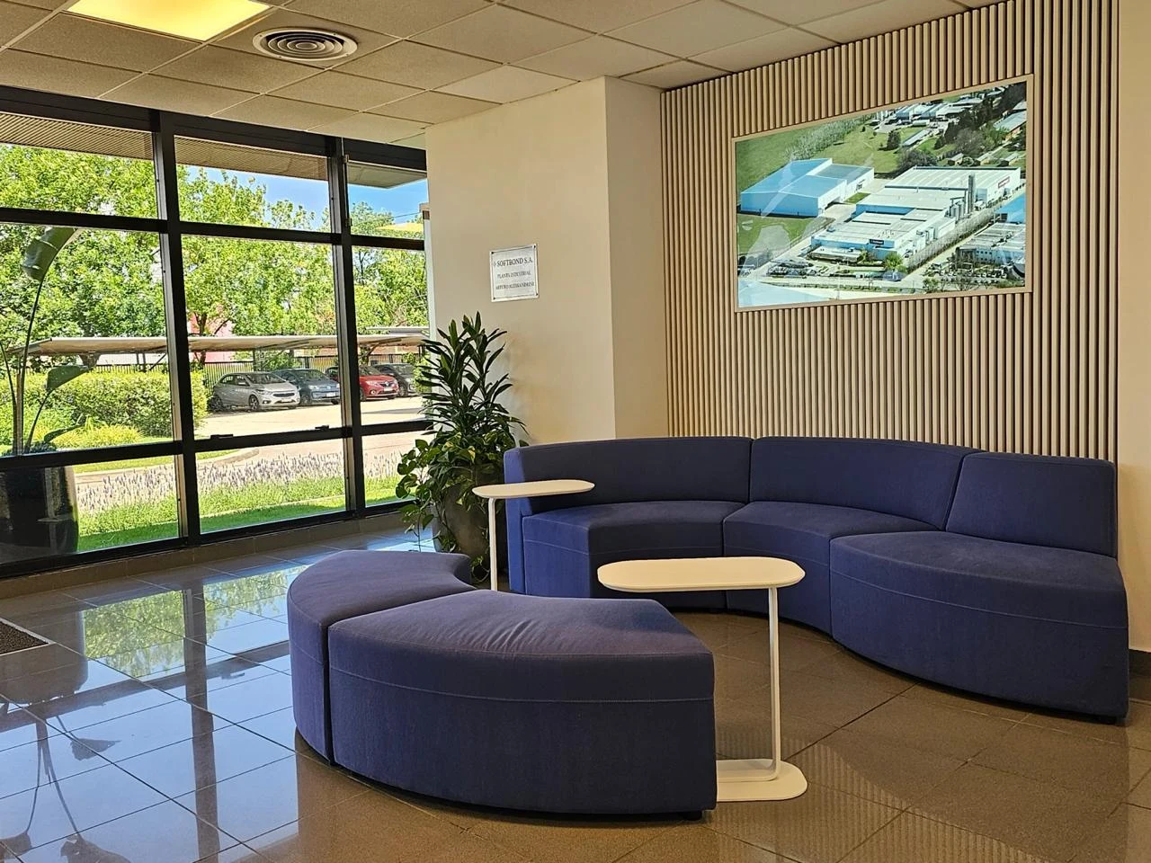 Recepción con sillones curvos azules, mesas auxiliares claras, pared de listones y grandes ventanales